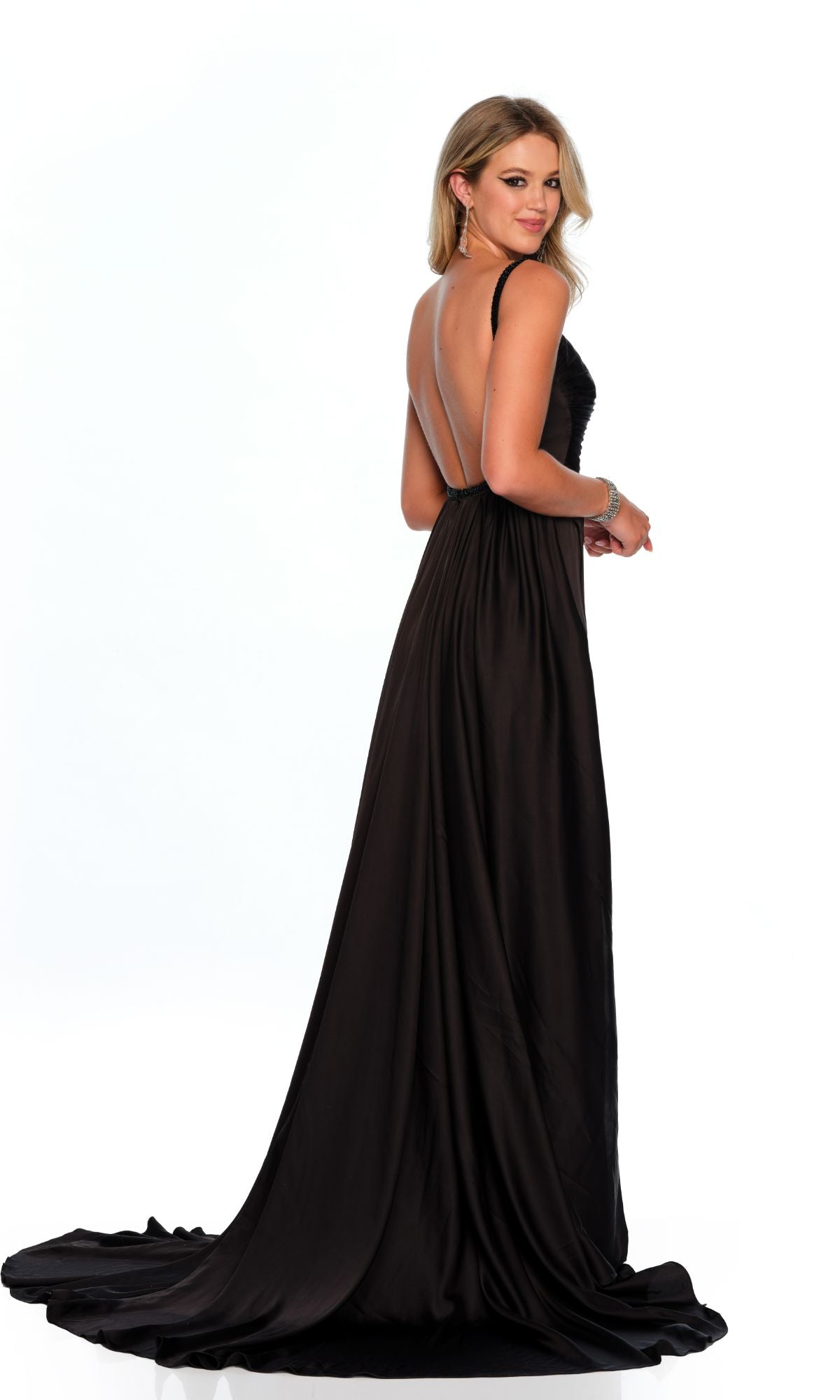 A woman with blonde hair models the Dave & Johnny 11514 long black prom dress, which features a deep open back. She faces away and glances over her shoulder, set against a white background.